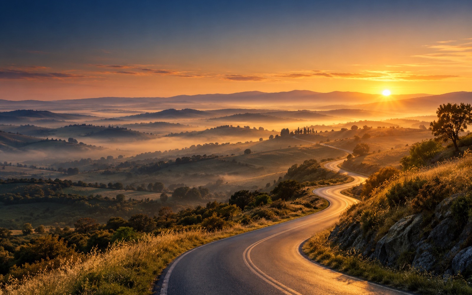 A winding road through misty rolling hills toward a golden sunrise